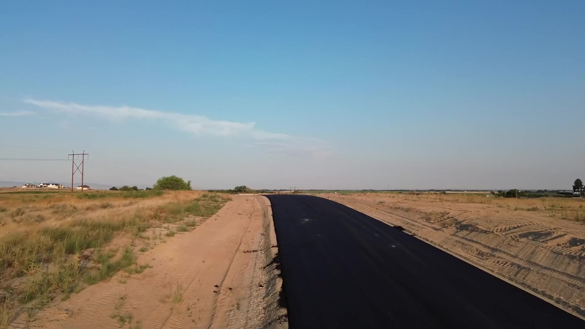 Drone view down a freshly paved street at The Stadium, with open sage and dry grassland under a clear sky